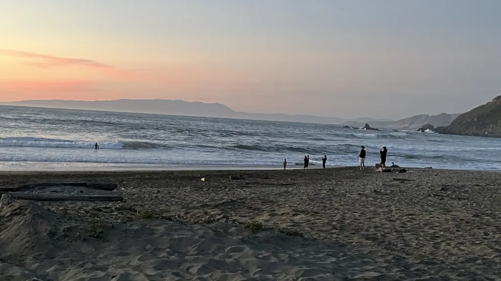 Sunset at a Pacifica beach with people near the shoreline and waves along the California coast
