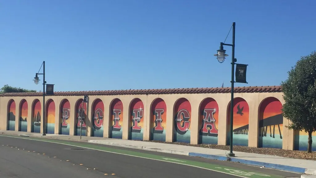 Colorful Pacifica mural on Palmetto Avenue in Pacifica, California, featuring sunset scenes and the word PACIFICA painted across arched panels.