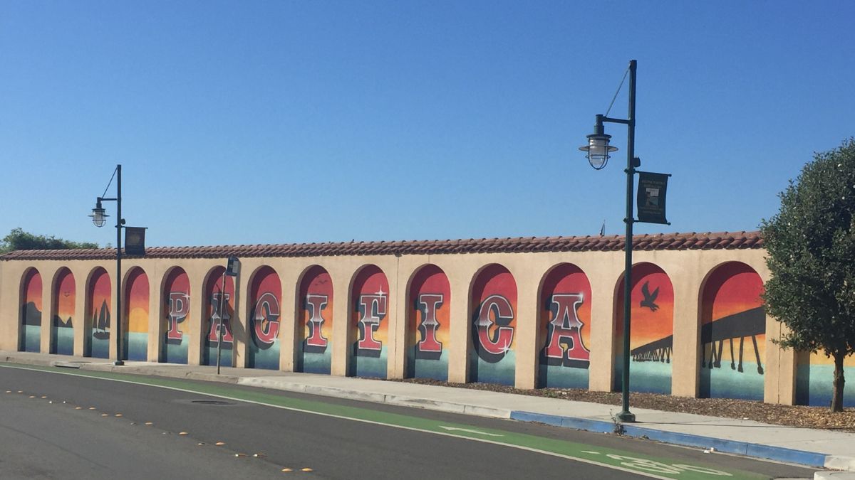 Colorful Pacifica mural on Palmetto Avenue in Pacifica, California, featuring sunset scenes and the word PACIFICA painted across arched panels.