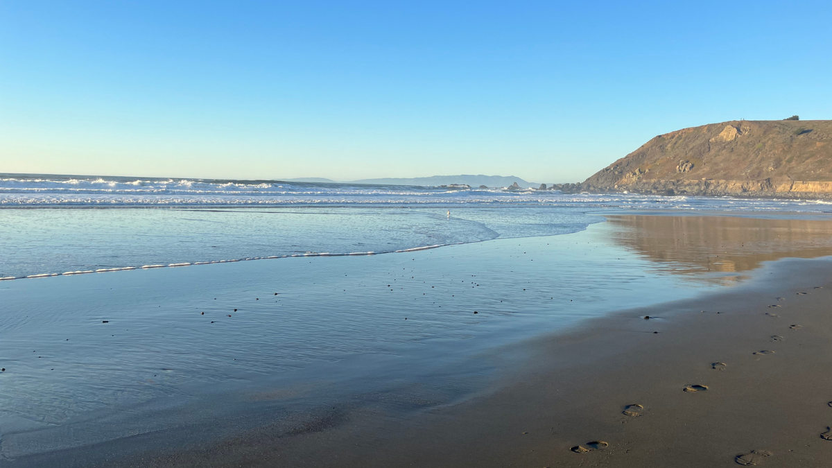 Pacifica State Beach shoreline with waves, wet sand reflections, and coastal cliffs along the San Mateo County coast