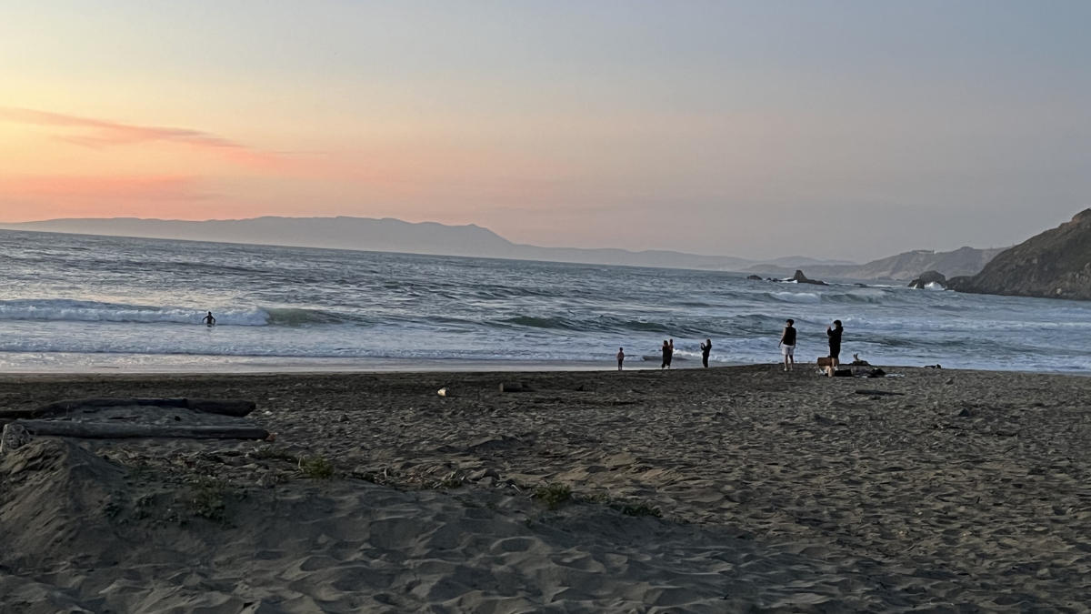 Sunset at a Pacifica beach with people near the shoreline and waves along the California coast